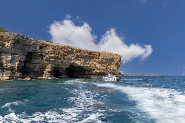 Polignano a Mare, İtalya, Apulia - 24 Mayıs 2024: Adriyatik Denizi kıyısındaki pitoresk uçurumların suyundan görüş. Turistler kayalıklardaki bir mağaraya tekne ile giderler.