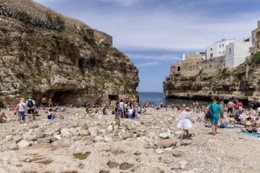 Polignano a Mare, Italy, Apulia - May 24, 2024: Lama Monachile beach, located between picturesque cliffs by Adriatic Sea. People relaxing on stone shore and swimming in the water clipart