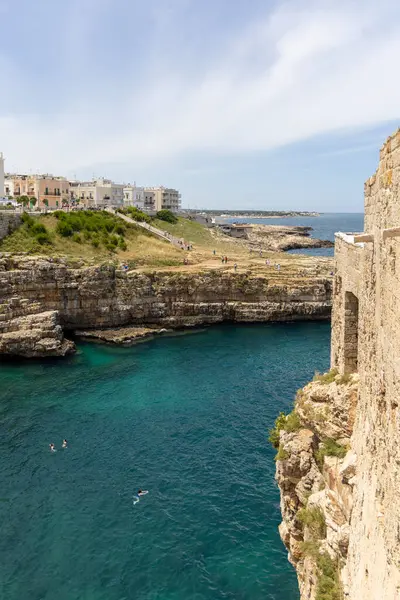 Polignano a Mare, İtalya, Apulia - 24 Mayıs 2024: Adriyatik Denizi kıyısındaki kayalıklar arasında yer alan Lama Monachile plajı. İnsanlar Grotta Piana yakınlarında suda yüzüyor.