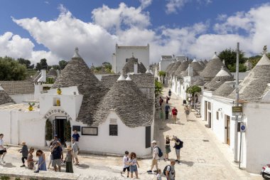 Alberobello, Apulia, İtalya - 21 Mayıs 2024: Trulli evleri, geleneksel, eşsiz, konik çatısı olan Apulian kuru taş barakası. Tarihi bir kasabanın caddelerinden birinde yürüyen turistler