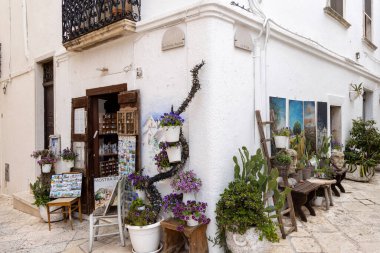 Locorotondo; İtalya; Apulia - 20 Mayıs 2024: Akdeniz ülkelerinin tipik dükkanlarında sergilenen Picturesque Caddesi. Karakteristik pürüzsüz, parlak taş kaldırım ve çiçekli saksılar.