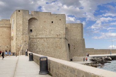 Monopoli, İtalya, Apulia - 21 Mayıs 2024: Ortaçağ Charles Şatosu (Castello Carlo V). İnsanlar Adriyatik Denizi 'ndeki pitoresk kıyı şeridi boyunca yürüyor