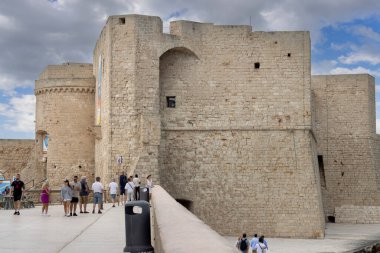 Monopoli, İtalya, Apulia - 21 Mayıs 2024: Ortaçağ Charles Şatosu (Castello Carlo V). İnsanlar Adriyatik Denizi 'ndeki pitoresk kıyı şeridi boyunca yürüyor