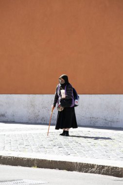 Vatikan, Roma, İtalya - 9 Ekim 2020: Yürüyen bir sopayla fakir giyimli dilenci yaşlı kadın, İtalya-Vatikan sınır duvarı karşısında para istiyor