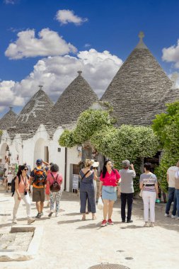 Alberobello, Apulia, İtalya - 21 Mayıs 2024: Trulli evleri, geleneksel, eşsiz, konik çatısı olan Apulian kuru taş barakası. Tarihi bir kasabanın caddelerinden birinde yürüyen turistler