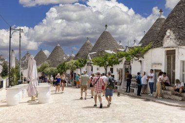 Alberobello, Apulia, İtalya - 21 Mayıs 2024: Trulli evleri, geleneksel, eşsiz, konik çatısı olan Apulian kuru taş barakası. Tarihi bir kasabanın caddelerinden birinde yürüyen turistler