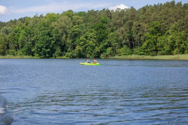 Masuria, Polonya - 24 Haziran 2020: Polonya Masuria Gölü, su üzerinde kanoyla gezen çift, ormanla kaplı kıyıya yakın