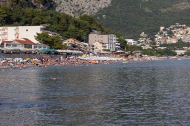 Sutomore, Karadağ - 25 Haziran 2023: Adriyatik Denizi kıyısında kumsal, birçok insan su kenarında dinleniyor. Çok popüler bir tatil köyüdür.