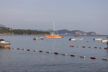 Sutomore, Karadağ - 25 Haziran 2023: Rumija dağlık yamacında Adriyatik Denizi kıyısı, demirlemiş tekne ve şehir manzarası. Burası popüler bir tatil beldesi.