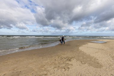 Miedzyzdroje, Wolin Adası, Polonya - 14 Eylül 2022: İnsanlar tatil sezonunun ardından rüzgarlı bir günde Baltık Denizi sahilinde yürüyorlar