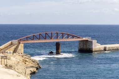 Valletta, Malta - 17 Nisan 2025: St. Elmo Köprüsü ve Saint Elmo Kalesi 'nden Grand Harbour' a kadar uzanan tarihi kırmızı çelik köprü, Akdeniz 'in mavi sularıyla çevrili.