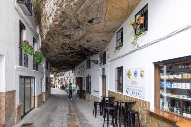 Setenil de las Bodegas, İspanya, Endülüs - 2 Nisan 2025: Uçurumun üzerindeki eşsiz beyaz köy kayalara inşa edildi. Cuevas de la Sombra Caddesi 'ndeki dar dükkan ve restoranlar.