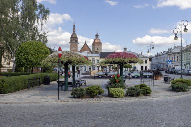 Nowy Sacz, Polonya - 30 Ağustos 2022: Güneşli bir günde dekoratif renkli çiçek düzenlemeleriyle Pazar Meydanı manzarası. Uzakta St. Malgorzata Üniversite Bazilikası 'nın kuleleri