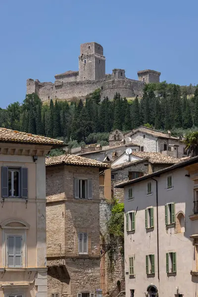 Assisi, İtalya - 12 Haziran 2025: Rocca Maggiore kalesinin manzarası, şehrin yukarısındaki tepedeki ortaçağ kalesinin kalıntıları. Önünde seramik çatıları olan eski taş binalar.