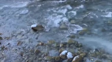 Dağ nehri. Güneşli bir günde, kristal gibi berrak bir dağ deresi karlı bir kış ormanında hızla akıyor. Karlar ve ağaç dalları ışıl ışıl karla kaplanarak dingin, doğal bir mucize yaratır..