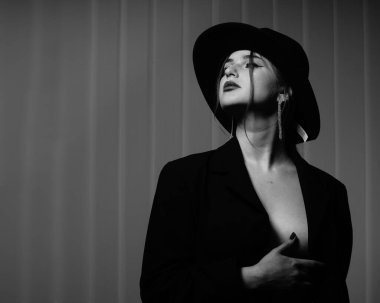 Stüdyoda poz veren siyah ceketli ve şapkalı güzel bir kızın siyah beyaz fotoğrafı.