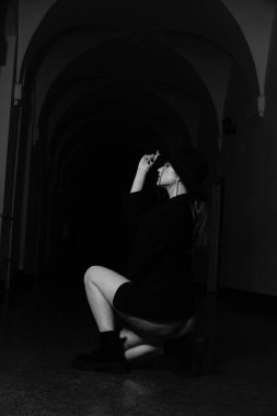 Stüdyoda poz veren siyah ceketli ve şapkalı güzel bir kızın siyah beyaz fotoğrafı.