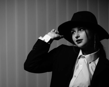 Stüdyoda poz veren siyah ceketli ve şapkalı güzel bir genç kızın siyah beyaz fotoğrafı.