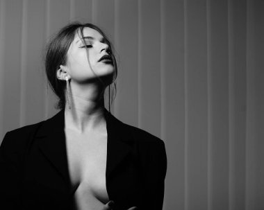 Stüdyoda çıplak bir şekilde poz veren siyah ceketli güzel bir kızın siyah beyaz fotoğrafı.