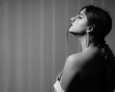 Stüdyoda çıplak bir şekilde poz veren beyaz tişörtlü güzel bir kızın siyah beyaz fotoğrafı.