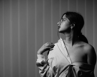 Stüdyoda çıplak bir şekilde poz veren beyaz tişörtlü güzel bir kızın siyah beyaz fotoğrafı.