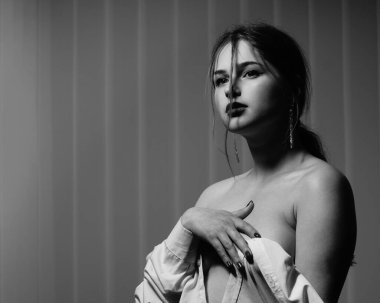 Stüdyoda çıplak bir şekilde poz veren beyaz tişörtlü güzel bir kızın siyah beyaz fotoğrafı.