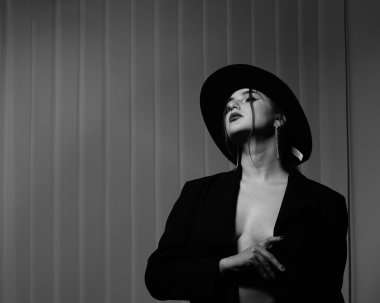 Stüdyoda poz veren siyah ceketli ve şapkalı güzel bir kızın siyah beyaz fotoğrafı.