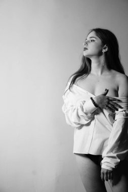 Stüdyoda çıplak bir şekilde poz veren beyaz tişörtlü güzel bir kızın siyah beyaz fotoğrafı.