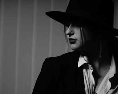 Stüdyoda poz veren siyah ceketli ve şapkalı güzel bir genç kızın siyah beyaz fotoğrafı.