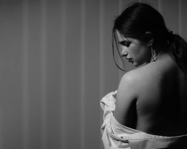 Stüdyoda çıplak bir şekilde poz veren beyaz tişörtlü güzel bir kızın siyah beyaz fotoğrafı.