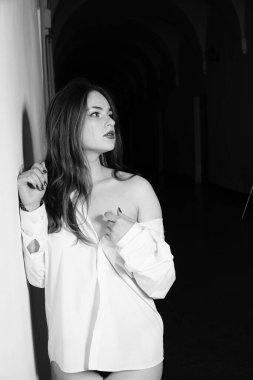 Stüdyoda çıplak bir şekilde poz veren beyaz tişörtlü güzel bir kızın siyah beyaz fotoğrafı.