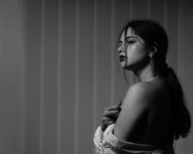 Stüdyoda çıplak bir şekilde poz veren beyaz tişörtlü güzel bir kızın siyah beyaz fotoğrafı.