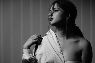 Stüdyoda çıplak bir şekilde poz veren beyaz tişörtlü güzel bir kızın siyah beyaz fotoğrafı.