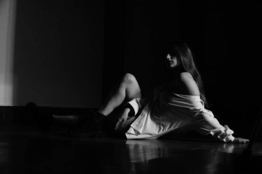 Stüdyoda çıplak bir şekilde poz veren beyaz tişörtlü güzel bir kızın siyah beyaz fotoğrafı.