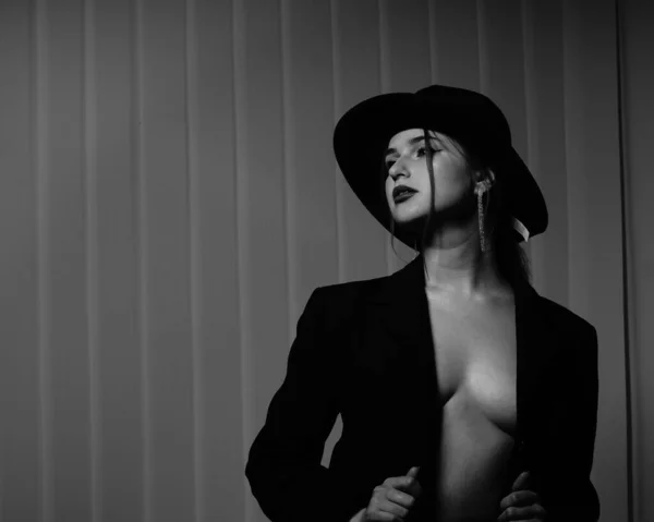 黒と白の美しい少女の写真1つだけ黒のブレザー彼女の裸の体と帽子の上に彼女のスタジオでポーズ — ストック写真