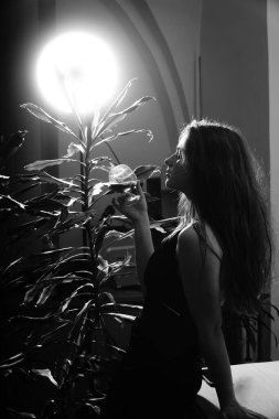 Siyah elbiseli güzel bir kadının siyah beyaz fotoğrafı. Bir bardak viski ile kameraya poz veriyor.