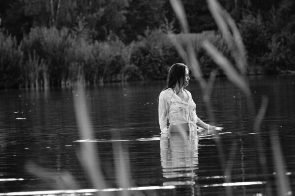 Black and white photo of a girl on a lake in the park. wet hair and clothes.