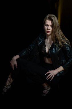 Stüdyoda siyah deri ceketli ve dantelli iç çamaşırlı genç bir kadın var.