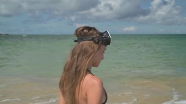 Model kahverengi bikinili ve elinde maskeyle tropikal bir adayı keşfeder. Kumsalın berrak suları, palmiye ağaçları ve sabah güneşinin ve egzotik dinginliğin sinemaları.