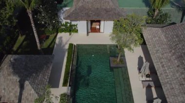 Sportif bir adam lüks bir villadan çıkar ve lüks bir villadaki havuzun yanındaki koltuklara oturur.