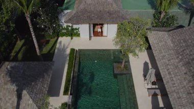 Sportif bir adam lüks bir villadan çıkar ve lüks bir villadaki havuzun yanındaki koltuklara oturur.