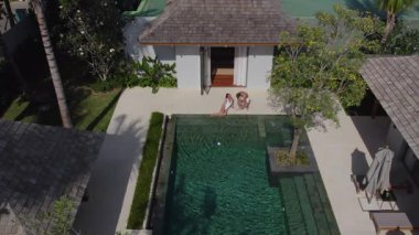 Lüks bir villada havuz başında oturan bir kız, sportif bir adam ona gelir.