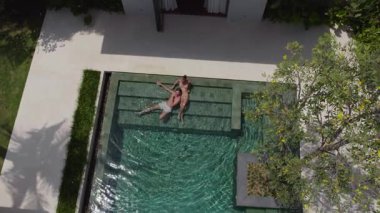 Bir erkek ve bir kız lüks bir havuzda birlikte yatıyorlar.