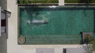 Sportif bir adam lüks bir villadan çıkar, temiz bir havuza dalar, suyun altında yüzer ve güzel bir kadının yanına çıkar. Canlı bir tropikal zarafet ve yaz enerjisi sahnesi..