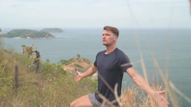 Dağda yoga yapan atletik bir adam uzak adaları olan sakin bir deniz manzarasına bakıyor. Tropikal, manzaralı bir ortamda sakin bir farkındalık anı.