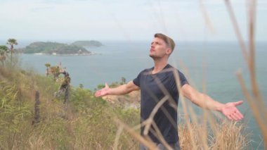 Dağda yoga yapan atletik bir adam uzak adaları olan sakin bir deniz manzarasına bakıyor. Tropikal, manzaralı bir ortamda sakin bir farkındalık anı.