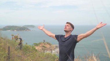 Dağda yoga yapan atletik bir adam uzak adaları olan sakin bir deniz manzarasına bakıyor. Tropikal, manzaralı bir ortamda sakin bir farkındalık anı.