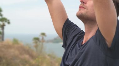 Dağda yoga yapan atletik bir adam uzak adaları olan sakin bir deniz manzarasına bakıyor. Tropikal, manzaralı bir ortamda sakin bir farkındalık anı.