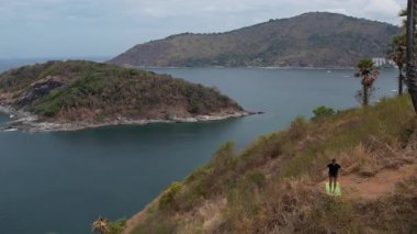 Uçurumun kenarında yoga yapan bir adam. İnsansız hava aracından çekilen çarpıcı okyanus ve ada manzaralı. Huzurlu, güçlü tropikal manzara.