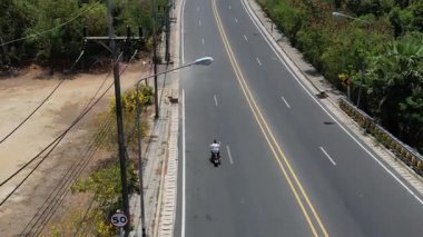 İnsanoğlu, okyanus manzaralı ve yakındaki adaları insansız hava aracı tarafından yakalanan dolambaçlı bir tropikal ada yolunda motosiklet sürüyor. Manzaralı ve maceralı.
